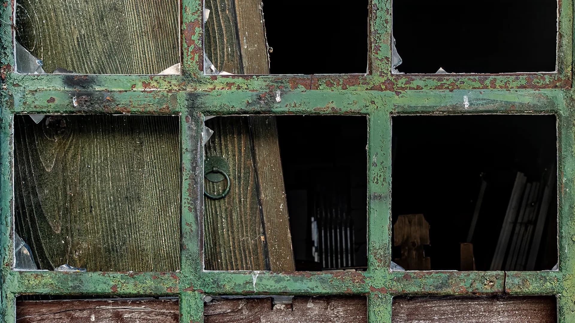 An abstract study of a rusted green window with broken panes.